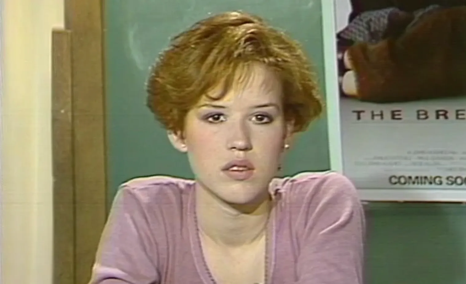 Young actress from 80s teen cinema with short red hair wearing a purple top in an indoor setting.