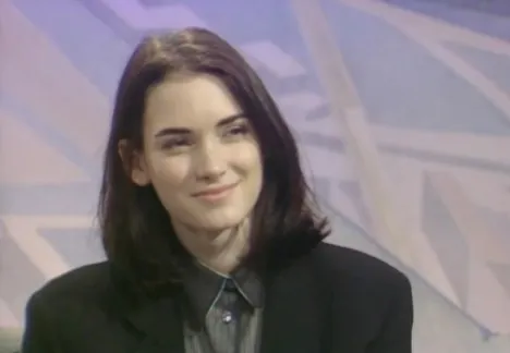 Young actress from quirky 80s teen and fantasy films with dark hair, wearing a black blazer and a subtle smile.