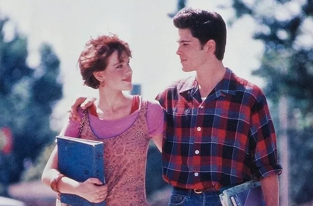 Young celebs from the 80s walking outside, holding books, starring in a John Hughes teen comedy scene.