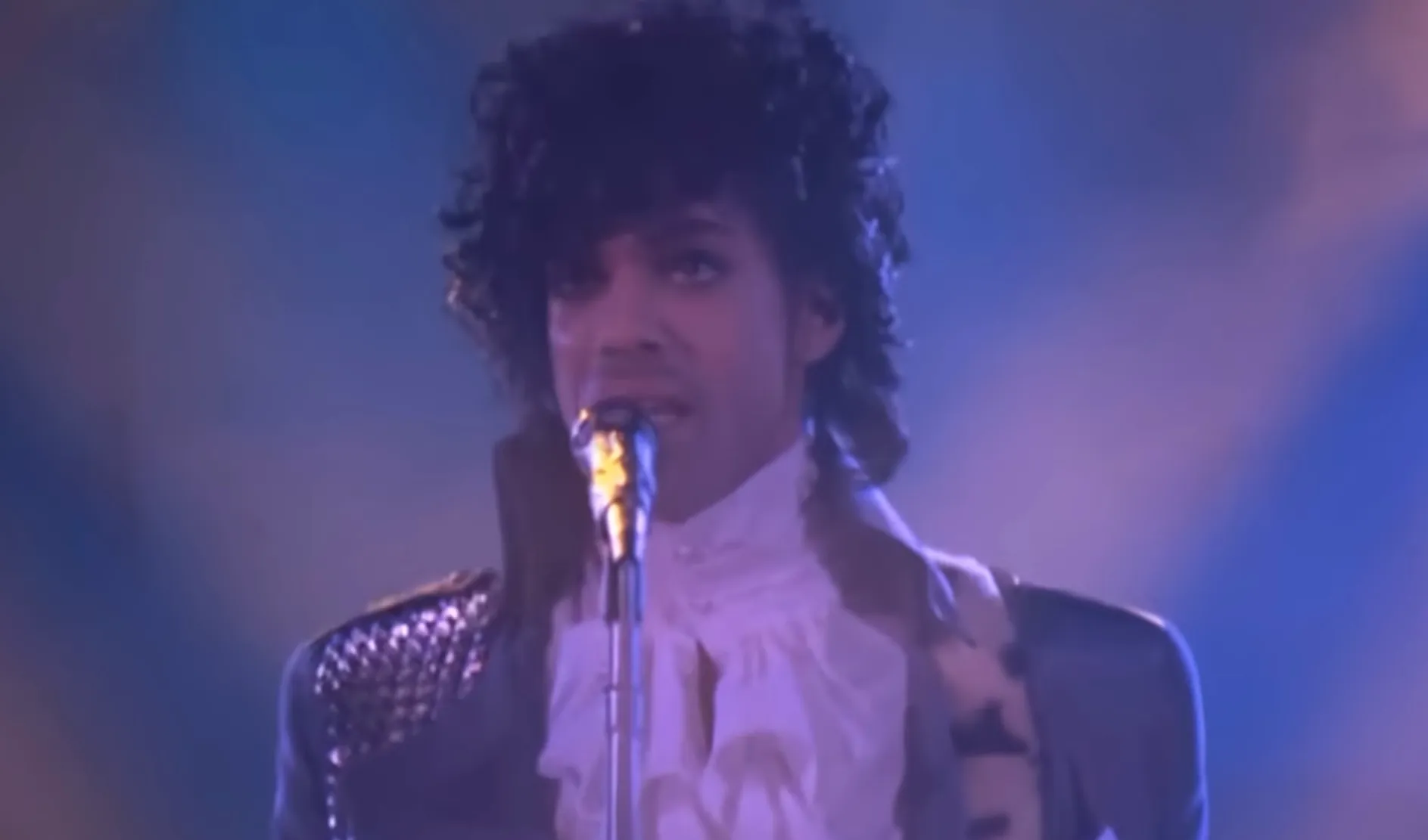 80s musician performing live on stage with ruffled shirt and dark curly hair, iconic celebs from the 80s.