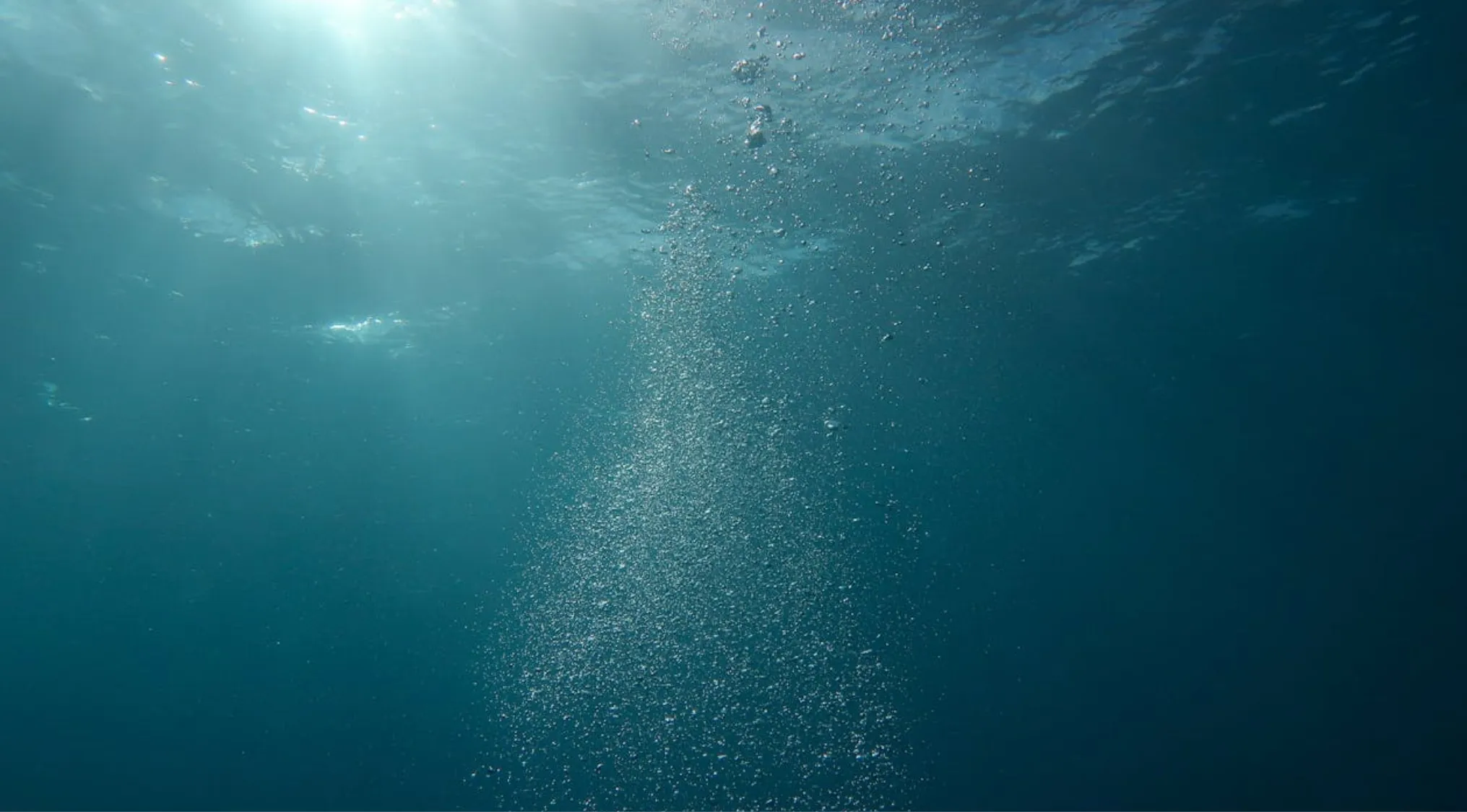 Underwater view of ocean depths with sunlight filtering through water and bubbles rising toward the surface.