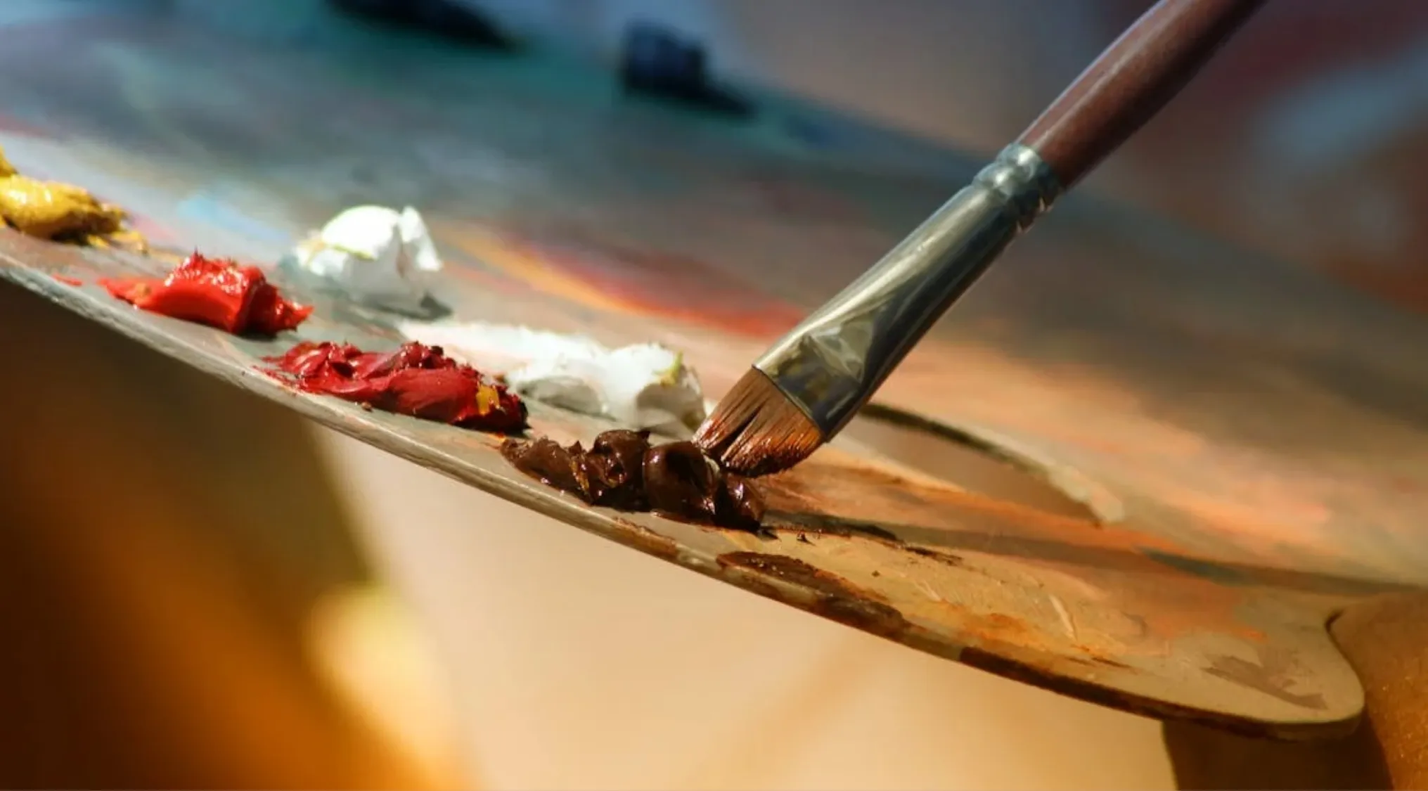 Artist mixing primary colors red, yellow, and blue on a palette to create secondary colors with a paintbrush.