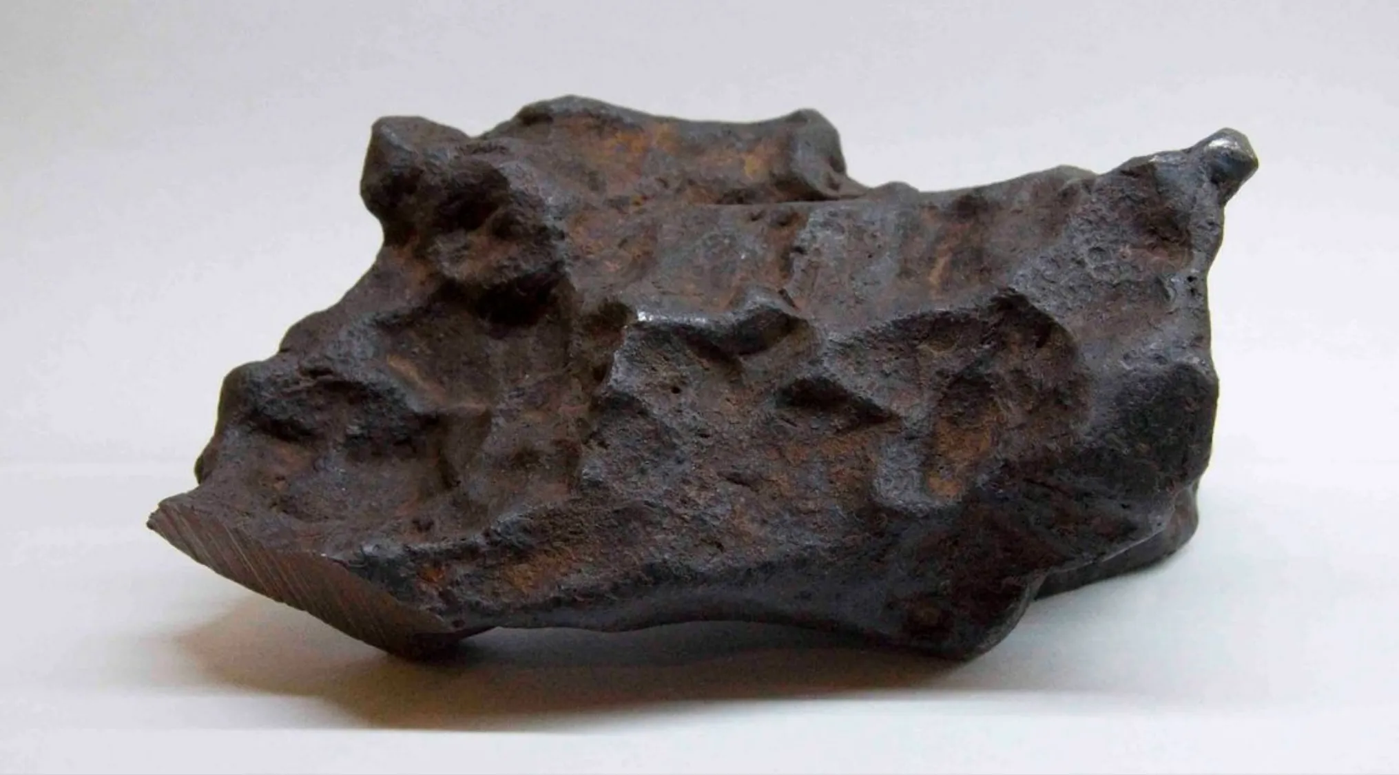 Dark rough meteorite rock from space that reached Earth's surface shown on a plain white background