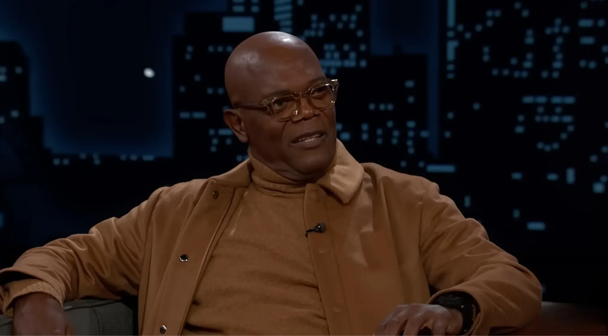 Samuel L. Jackson in a tan jacket and glasses during an interview guessing the movie from the side character role.