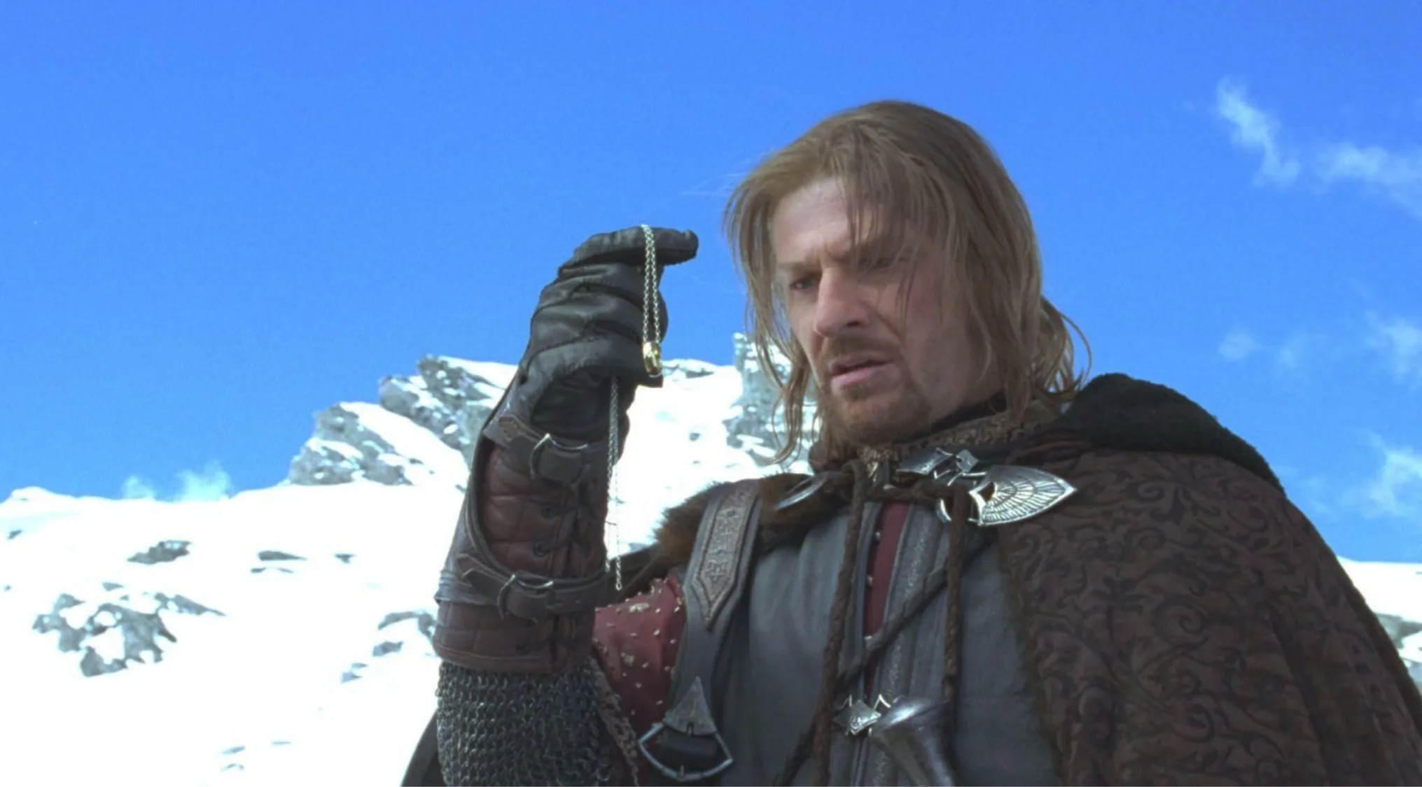 Side character from The Lord of the Rings holding the One Ring with snowy mountains in the background.