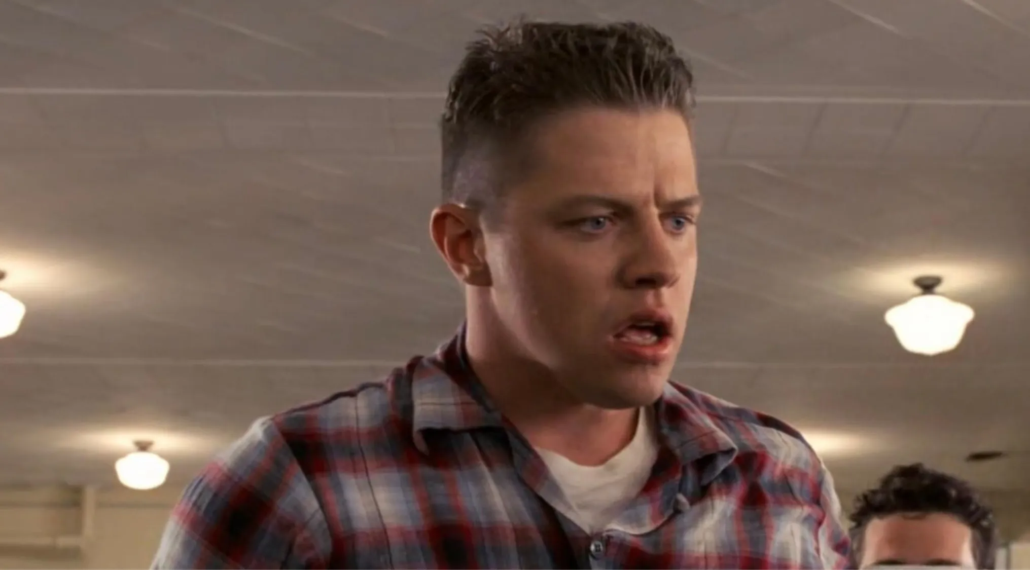 Side character from the movie looking intimidating but mostly ridiculous in a plaid shirt indoors.