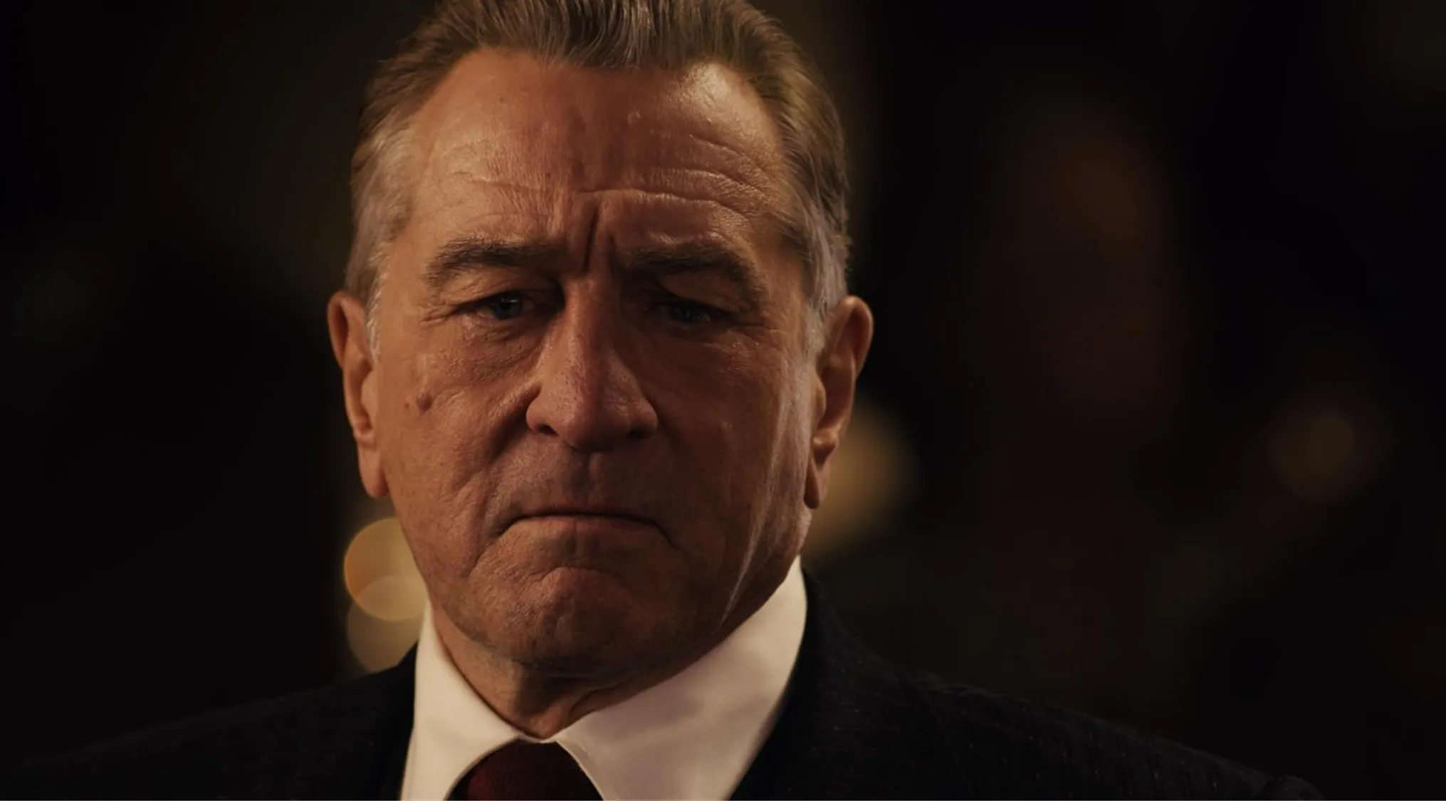 Robert De Niro as a side character in a dramatic movie scene, wearing a suit and tie, serious expression.