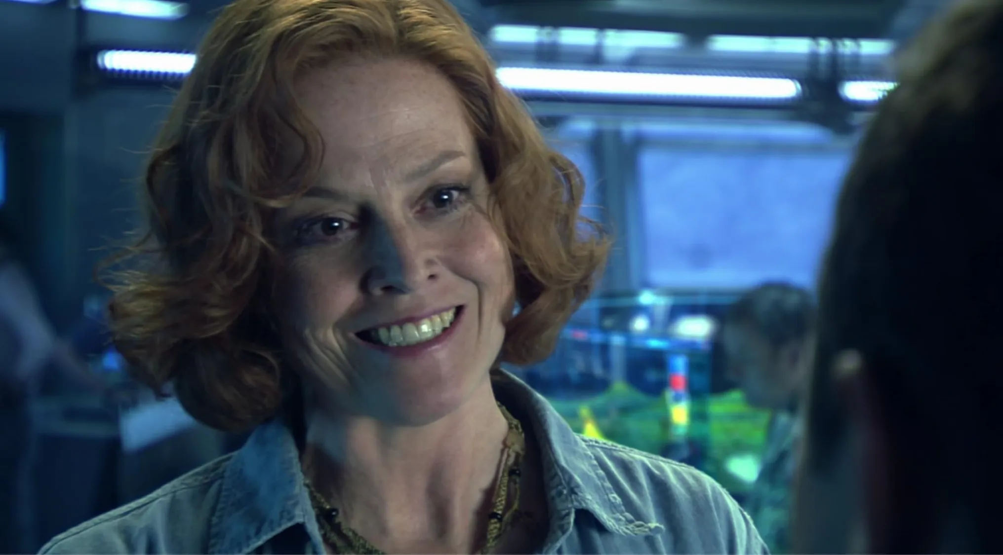 Side character from Avatar with curly red hair smiling inside a blue-lit futuristic setting.