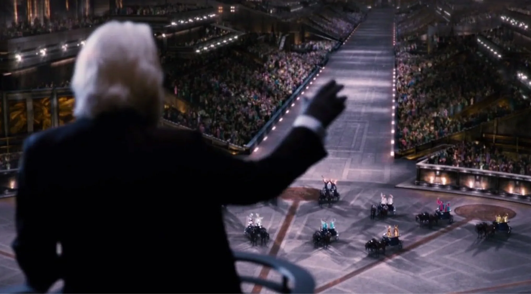 Side character in The Hunger Games waving to crowds during the arena tribute parade event.