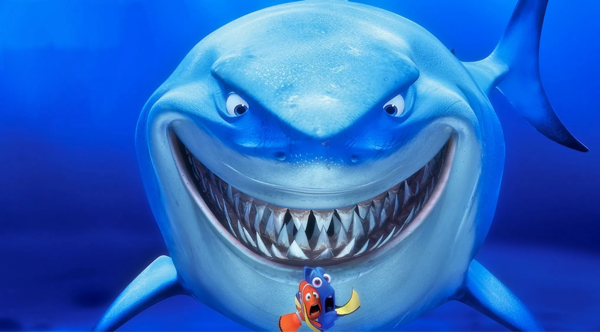 Animated shark character from Finding Nemo with sharp teeth swimming behind two smaller fish in the ocean.