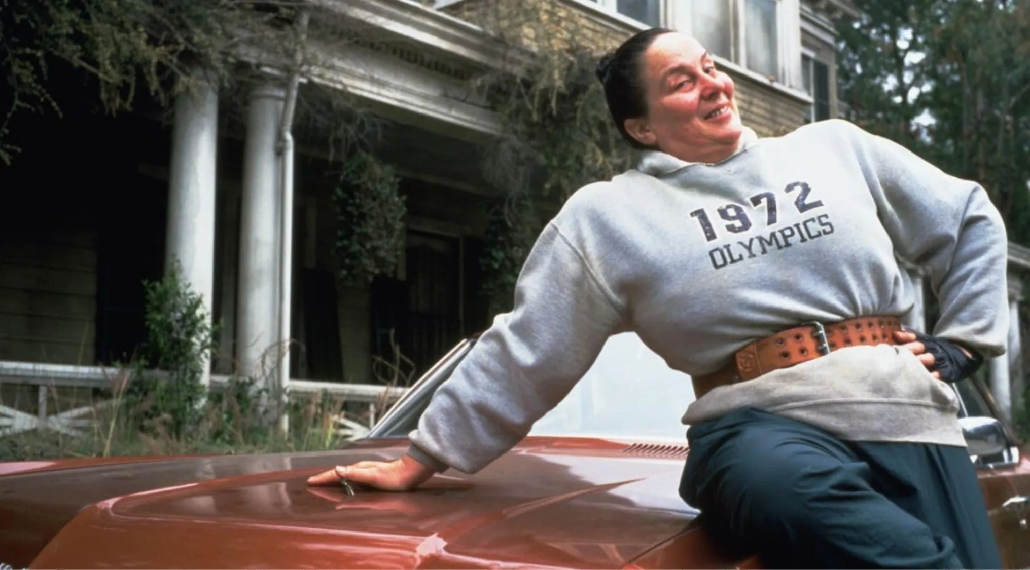 Terrifying headmistress side character leaning on car, known for strict rules and extreme punishments in the movie.