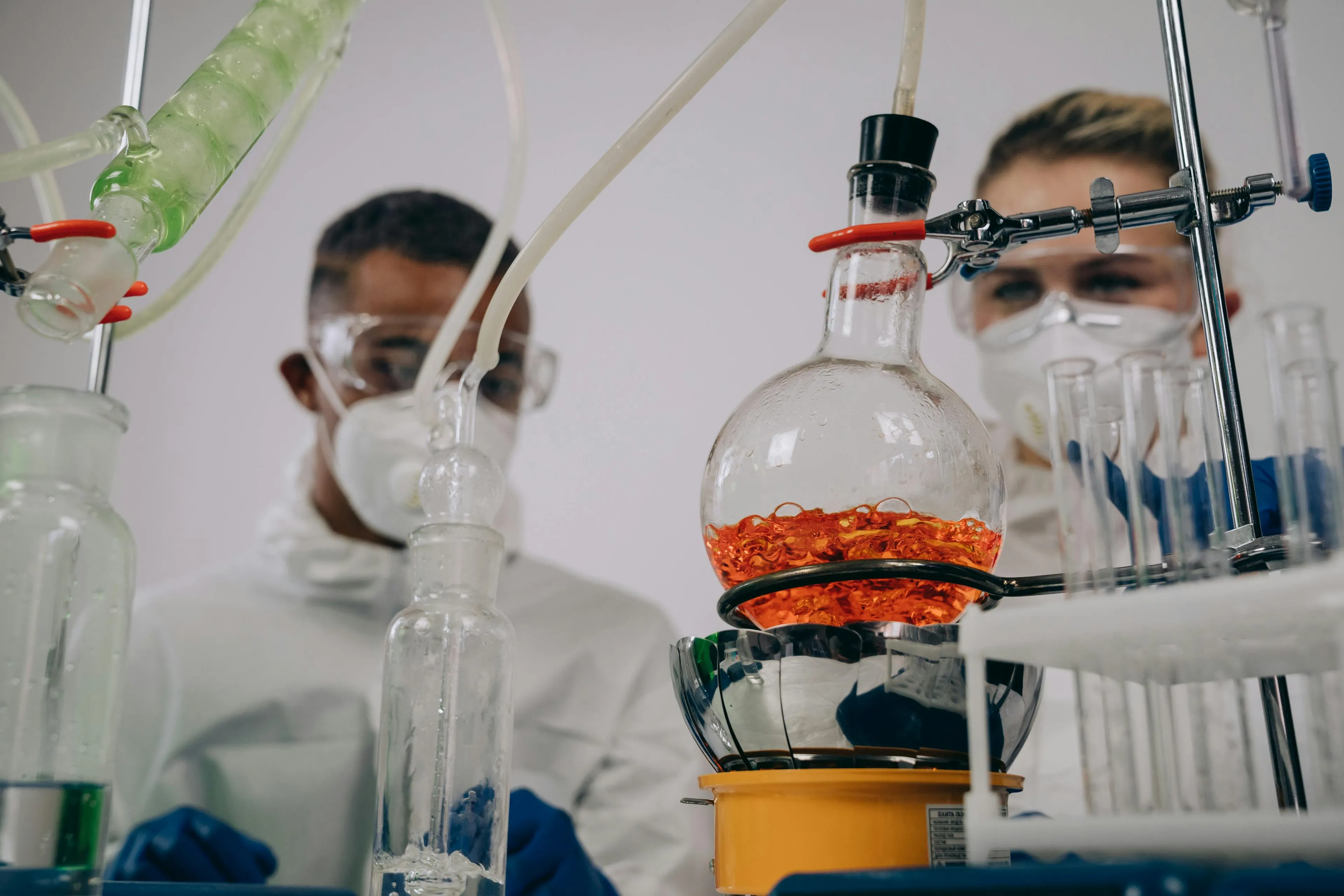 Two scientists in protective gear conducting chemical reactions with lab glassware demonstrating enzymes speeding up reactions.