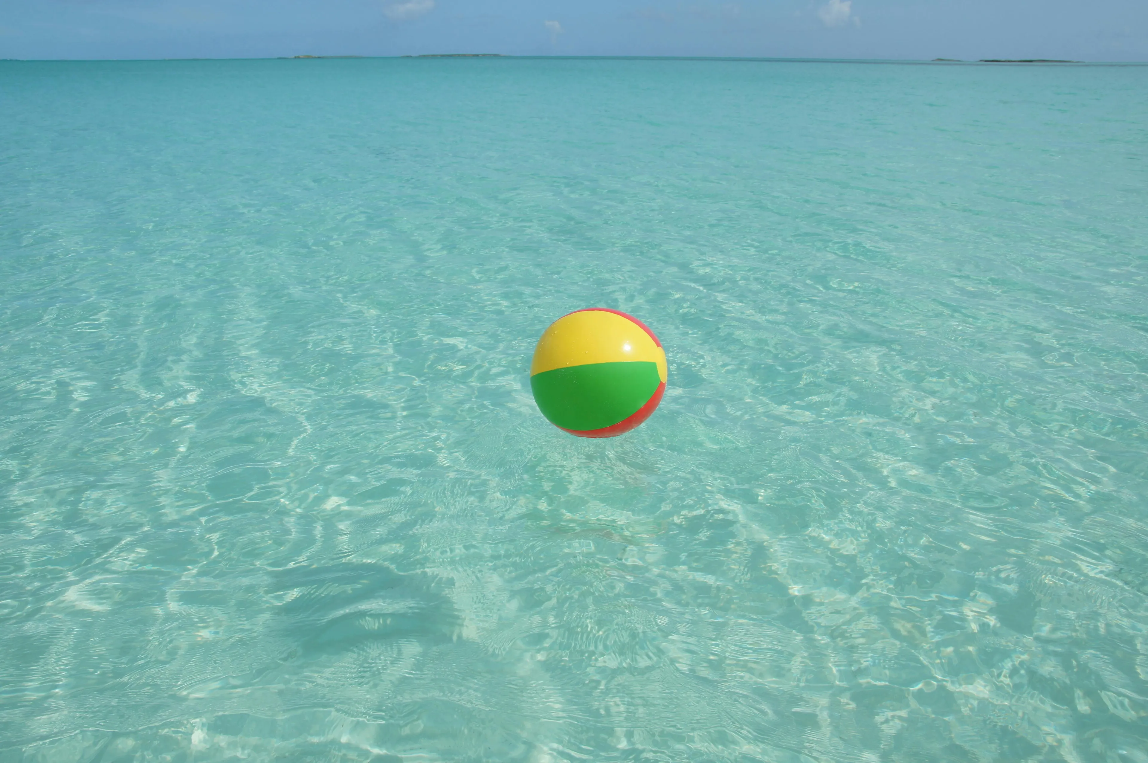 Colorful beach ball floating on clear turquoise water illustrating density as the measure of matter relative to volume.