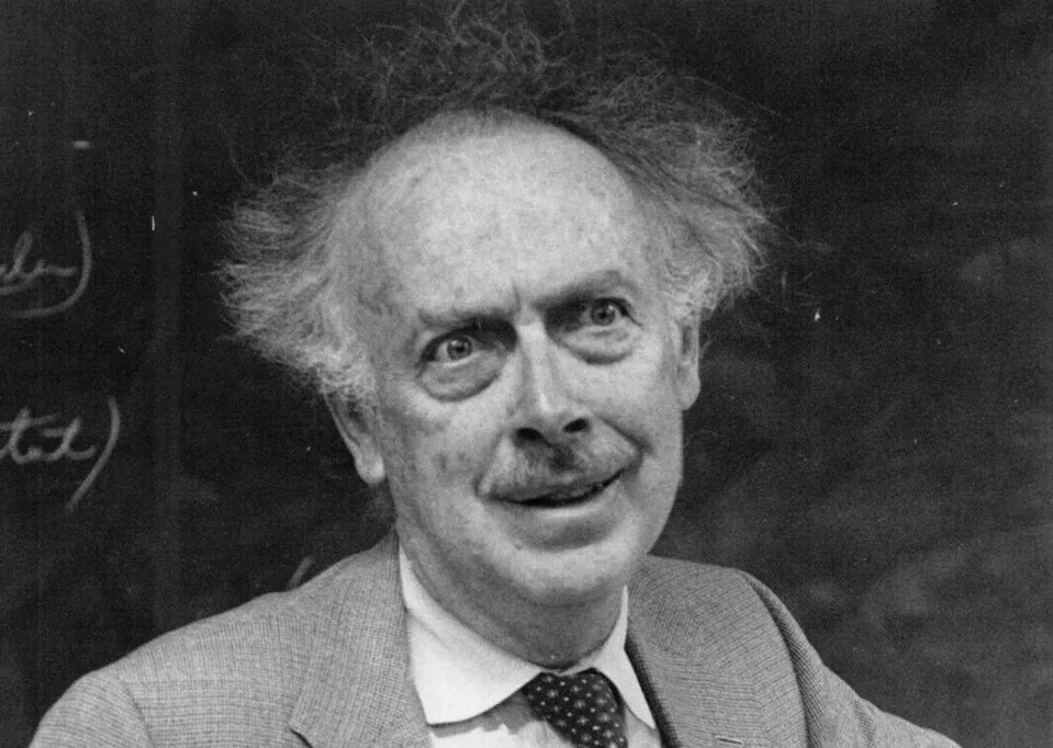 Scientist known as father of genetics with wild hair and mustache, wearing suit and tie in front of chalkboard.
