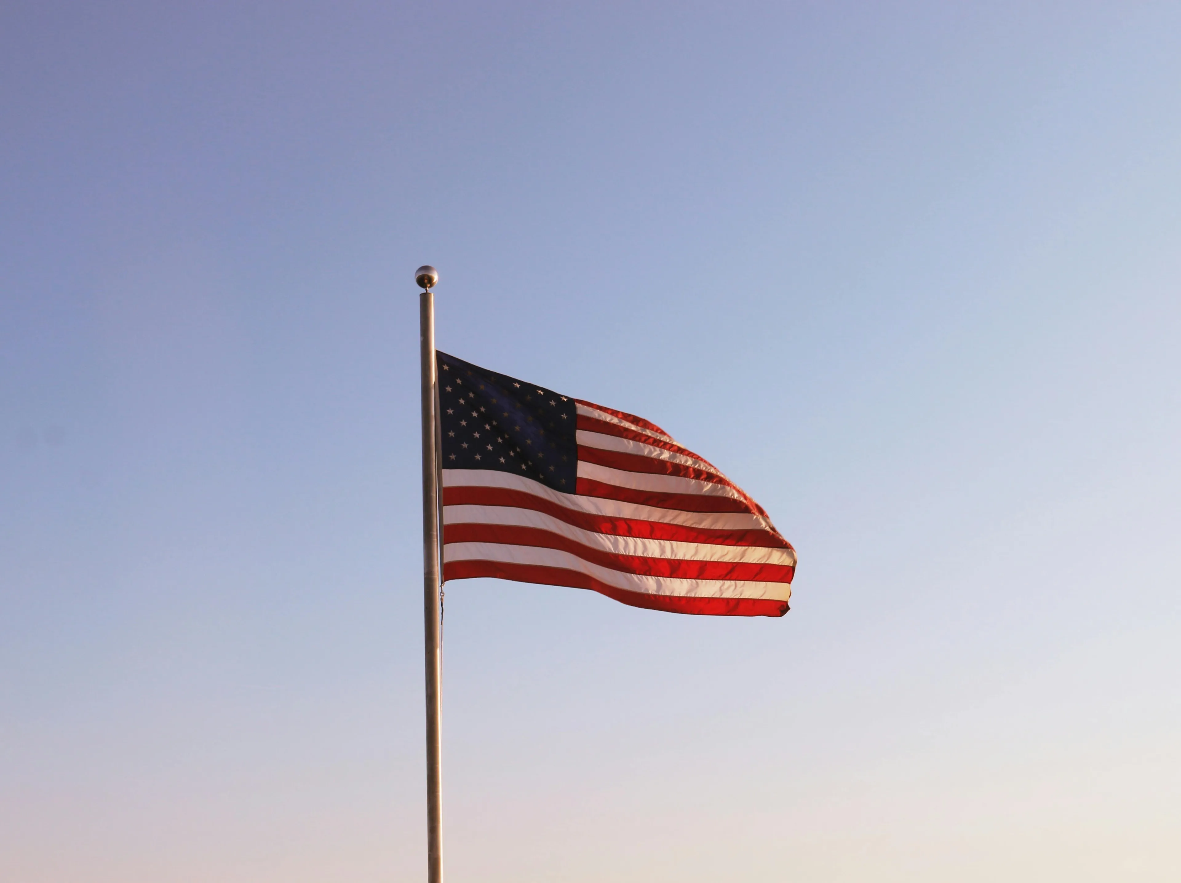 American flag waving on a pole against clear sky representing the $8,000 question on who was second president of the United States