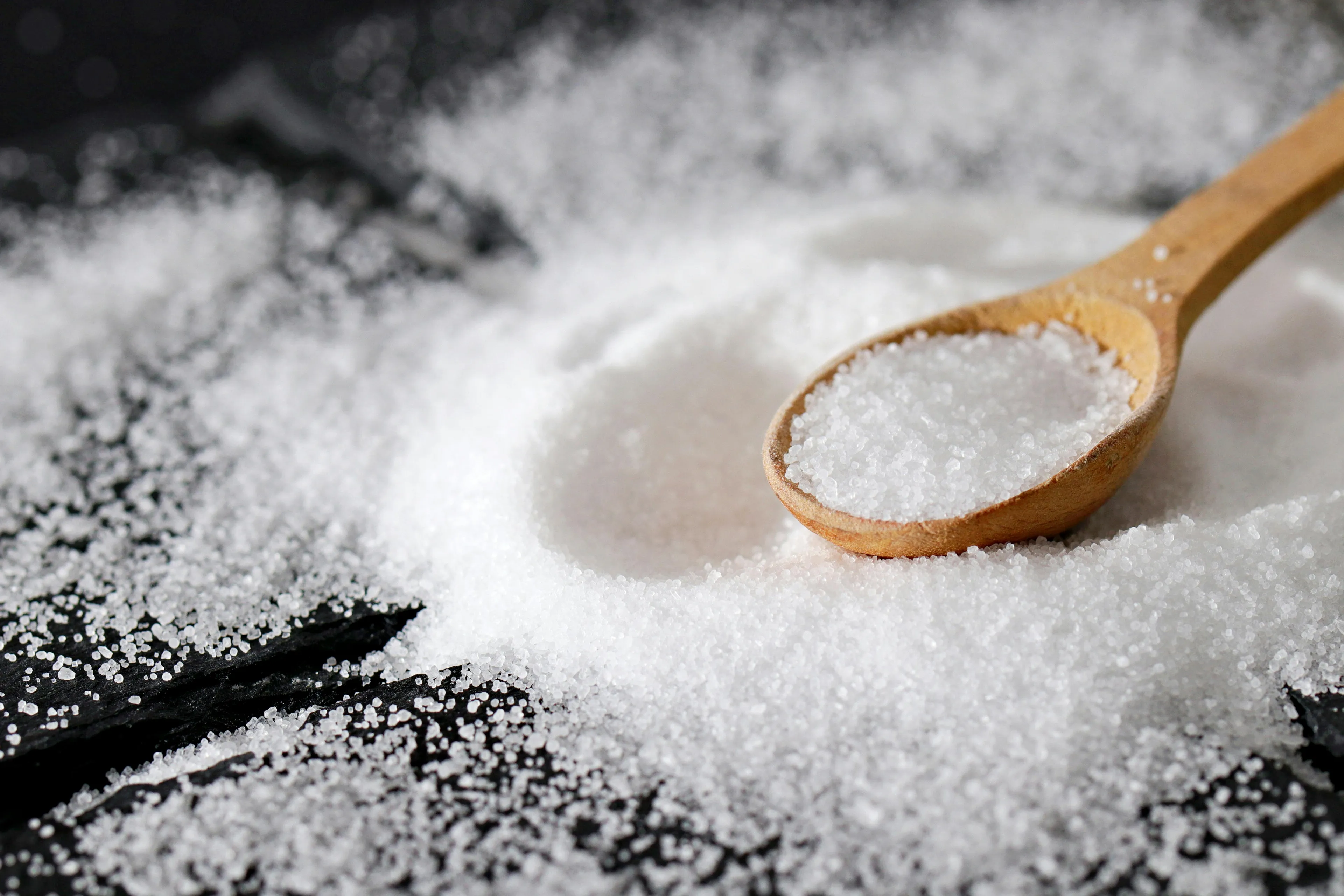 Close-up of table salt crystals in a wooden spoon, related to the chemical formula for table salt question.