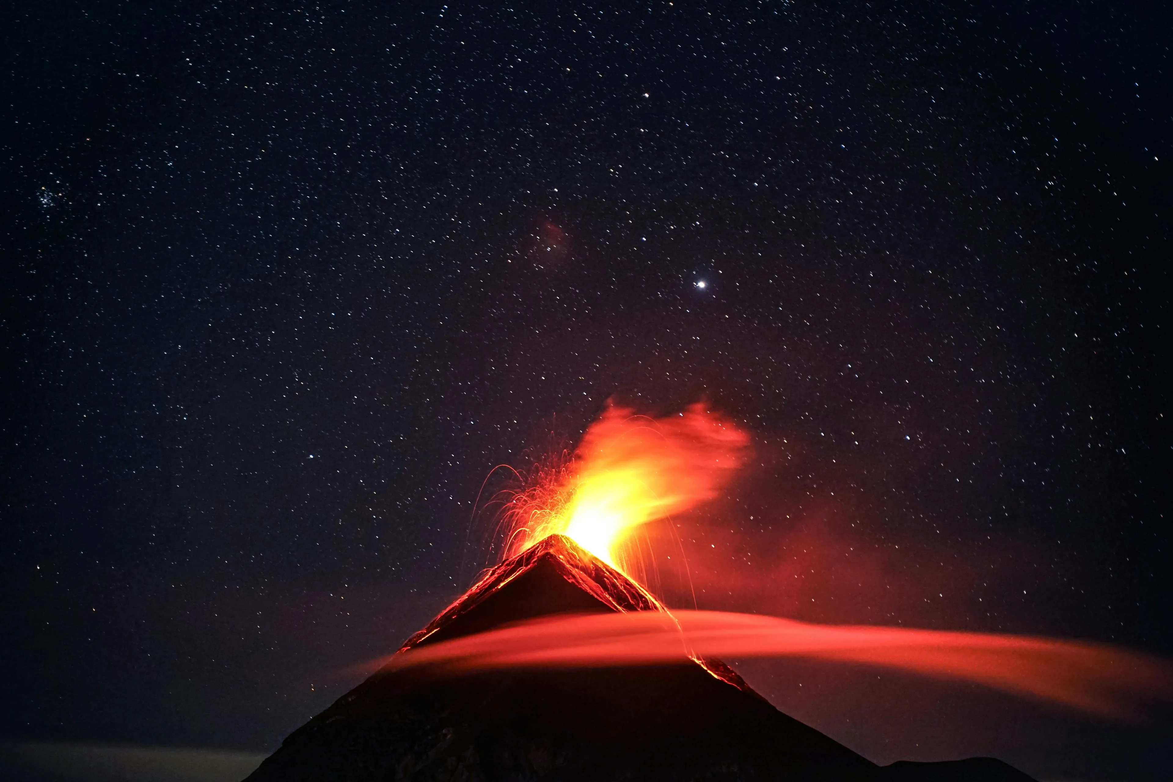 Erupting volcano at night under a starry sky, showing lava flow and volcanic eruption as the largest active volcano on Earth.