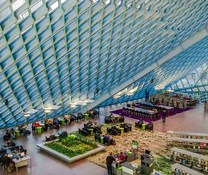 Modern and beautiful architecture of a large library interior with a glass ceiling, various seating areas, and people studying.