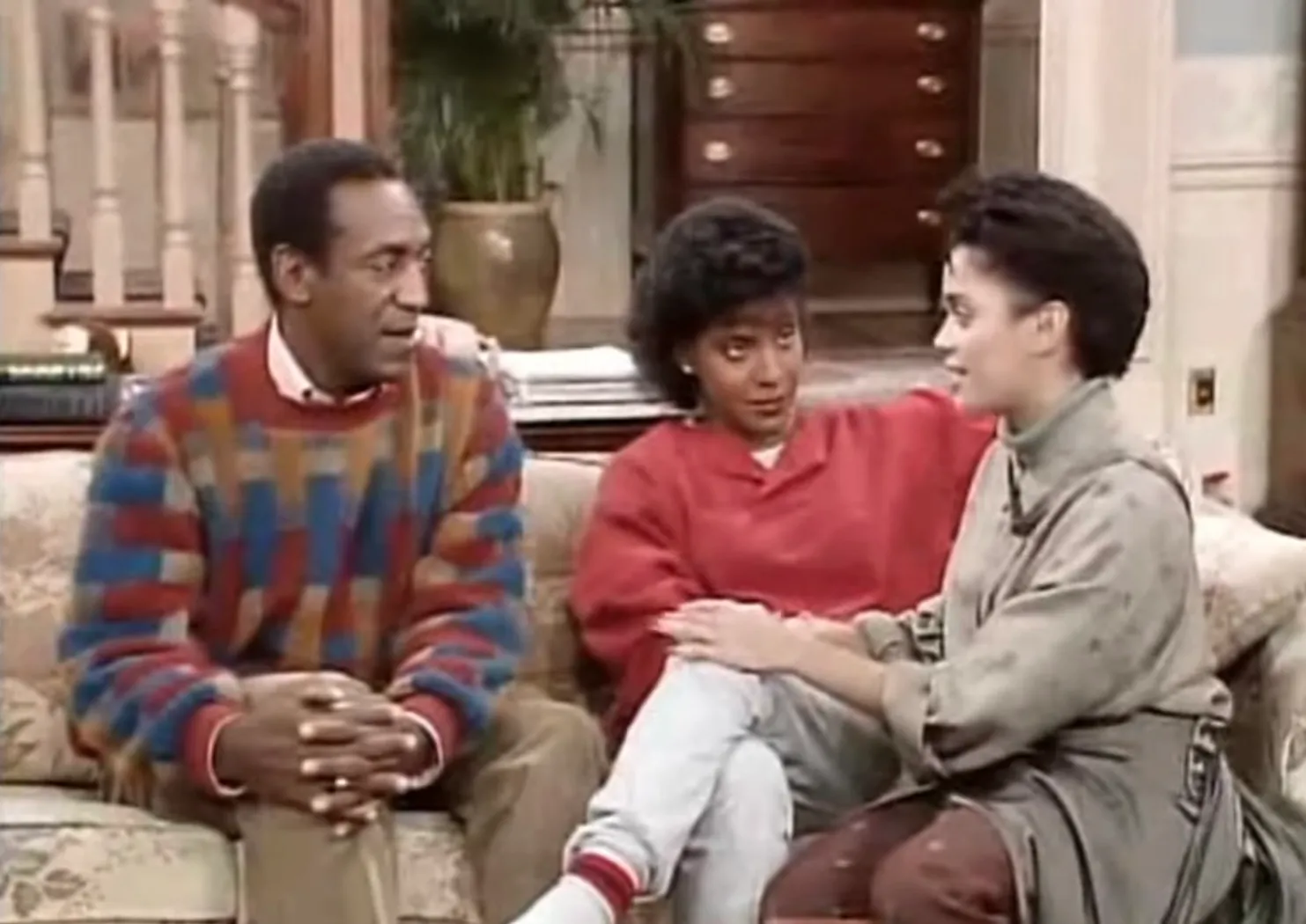 Three people sitting on a couch in a living room scene featuring the Huxtables family from television.