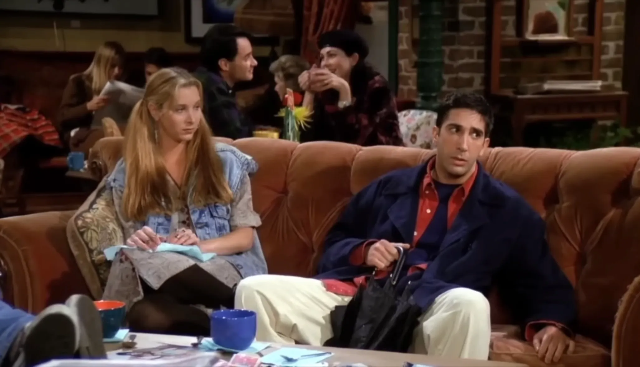 Main characters from Friends sitting on a couch inside the coffee shop where they frequently hang out.