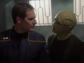 Captain Archer in Star Trek Enterprise uniform talks to an alien on a futuristic space station set.