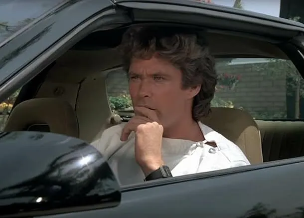 Man sitting in a black sports car, representing 80s and 90s TV knowledge in Knight Rider talking car trivia.