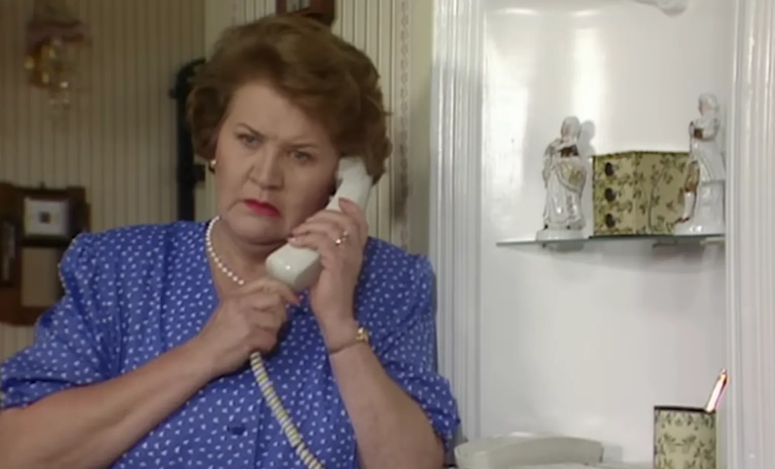 Hyacinth Bucket in classic 80s and 90s TV comedy, holding phone, known for correcting pronunciation of her last name.