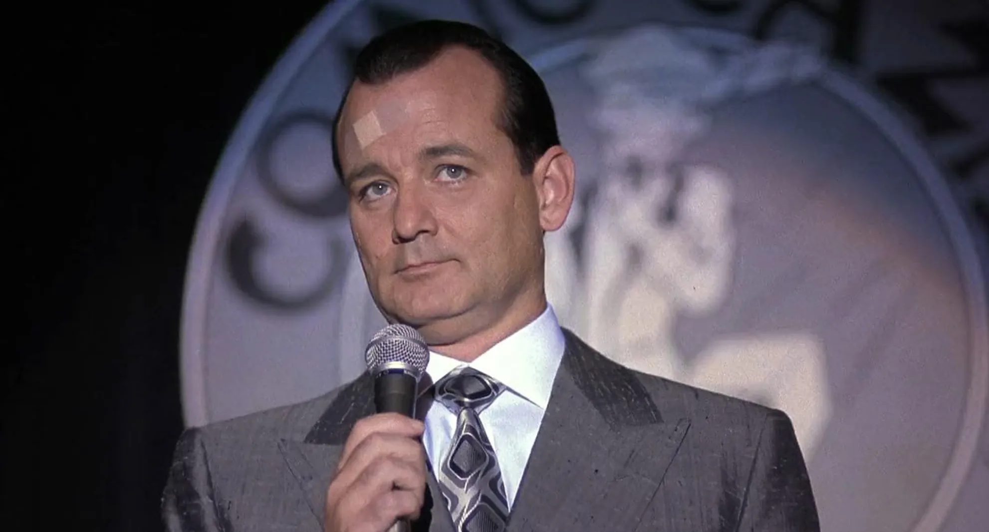 Actor holding a microphone wearing a suit and tie, representing a well-known actor from actors A-Z.