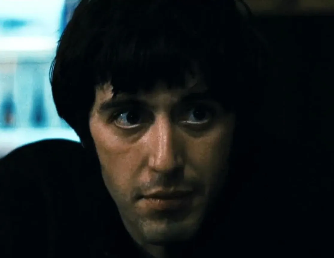 Al Pacino in a close-up scene from Scarface 1983, showing intense expression in low light setting.