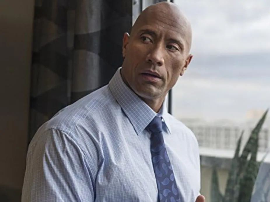 Dwayne Johnson wearing a shirt and tie, looking away thoughtfully, showcasing actor and WWE wrestler background.
