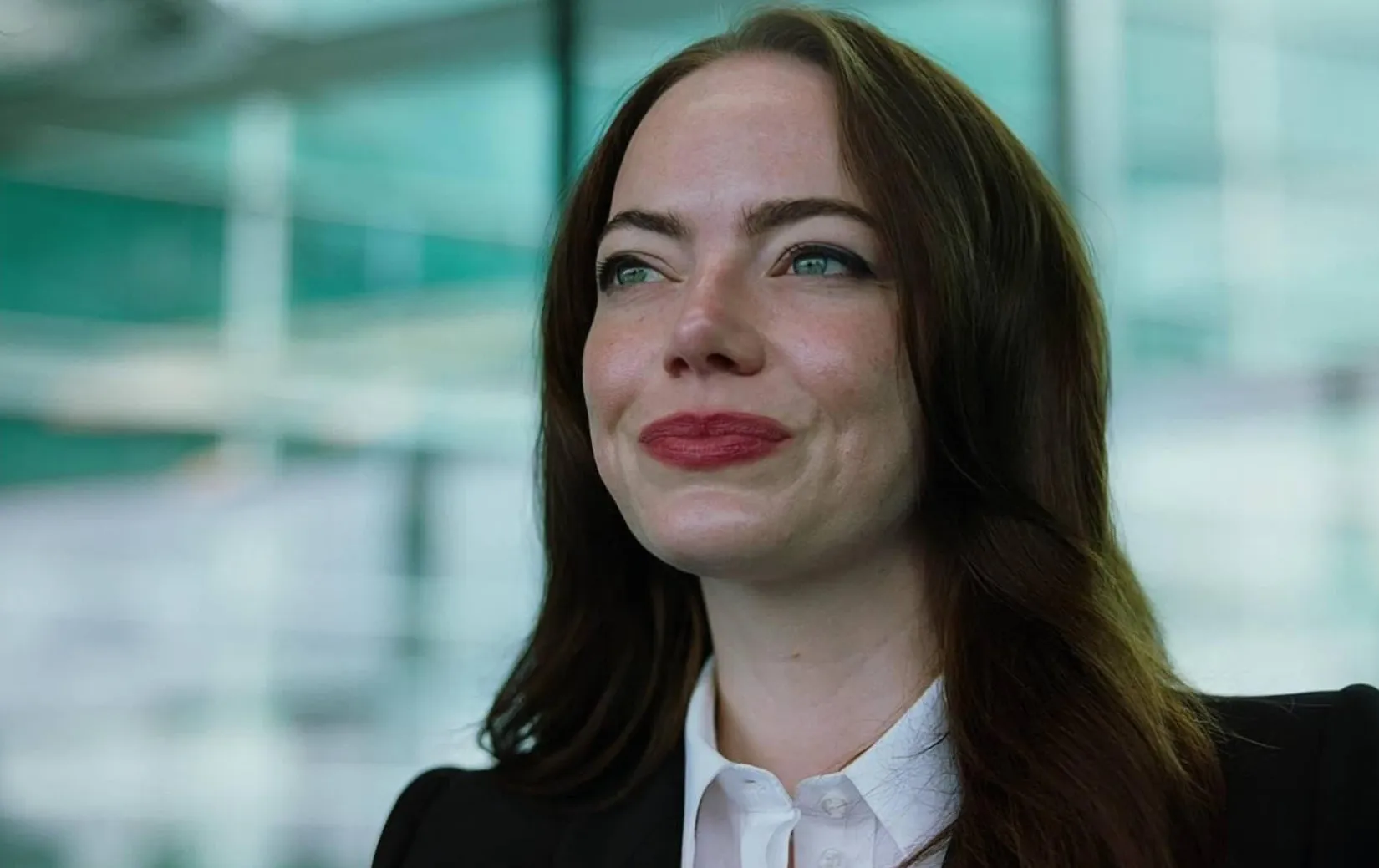 Famous actress with long dark hair and red lipstick smiling softly indoors with blurred modern background.