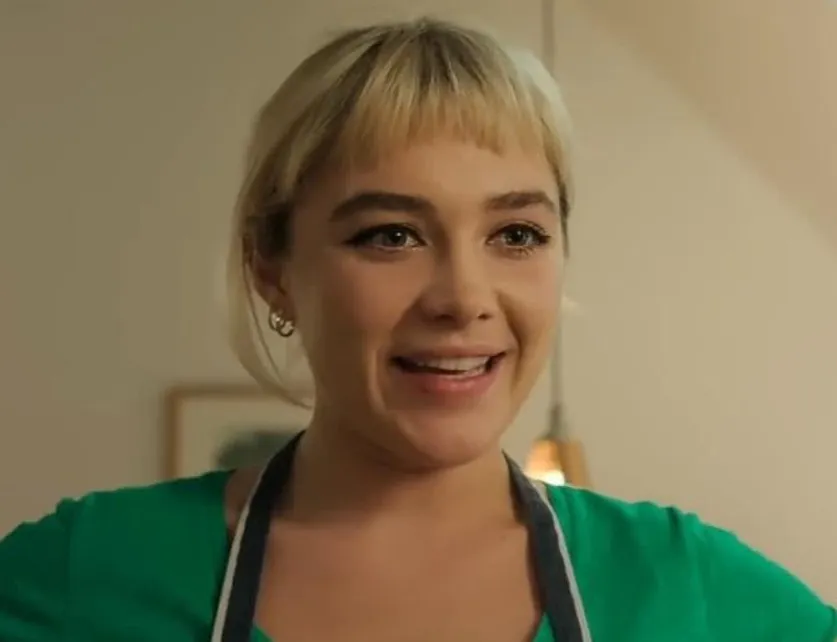 Florence Pugh smiling indoors, wearing a green top and apron, known for a lead role in Midsommar 2019.