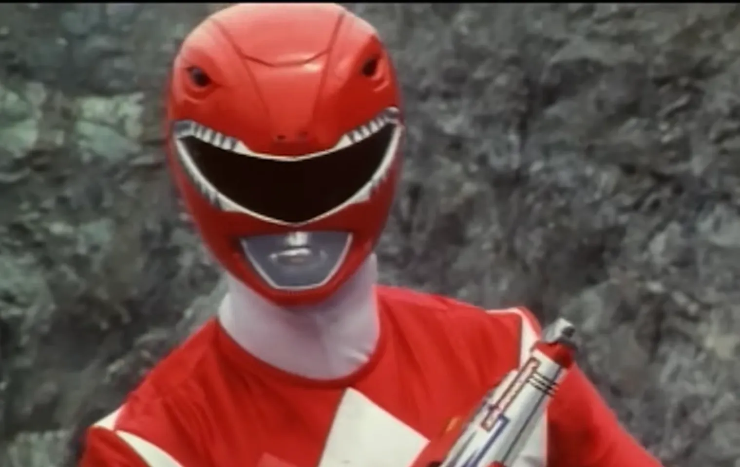 Red Ranger character from Power Rangers in original dinosaur-themed helmet and red suit holding a weapon outdoors.