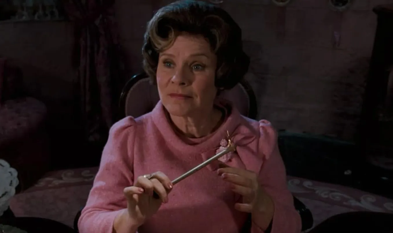Actress in a pink outfit holding a wand, embodying an infamous character in a dimly lit vintage room scene.