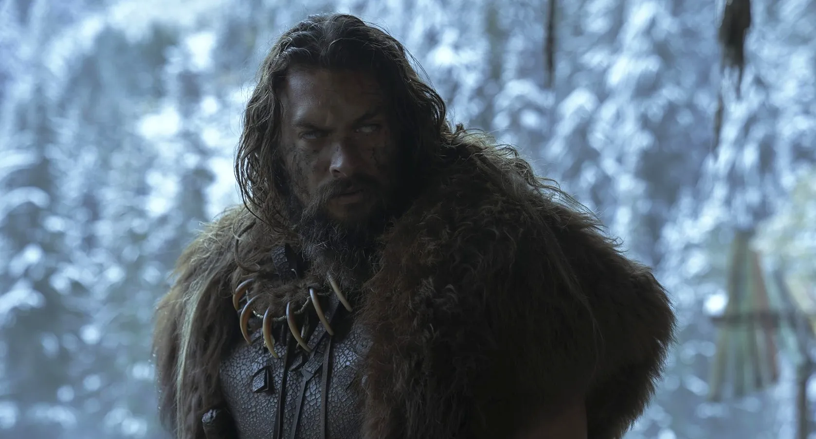 Actor in fur costume with long hair and beard in a snowy forest setting, embodying a rugged well-known actor character.