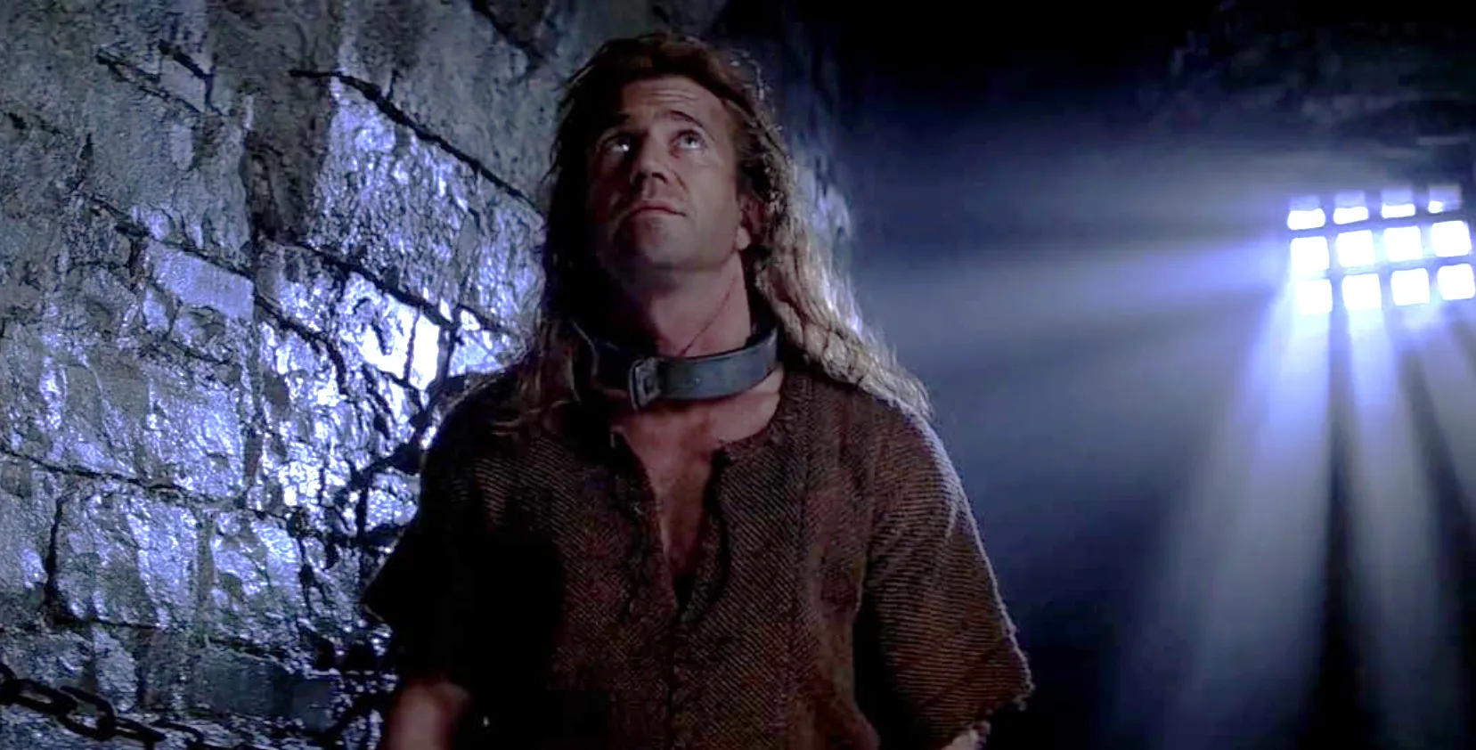 Famous actor in a medieval prison scene wearing a rough tunic and metal collar, light streaming through barred window.