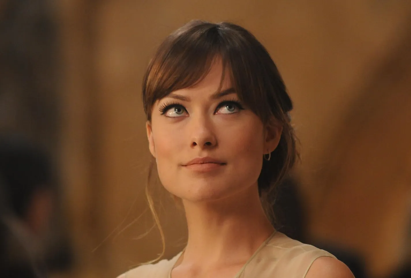 Olivia Wilde looking upward thoughtfully in a softly lit setting, known actress and talk show host.