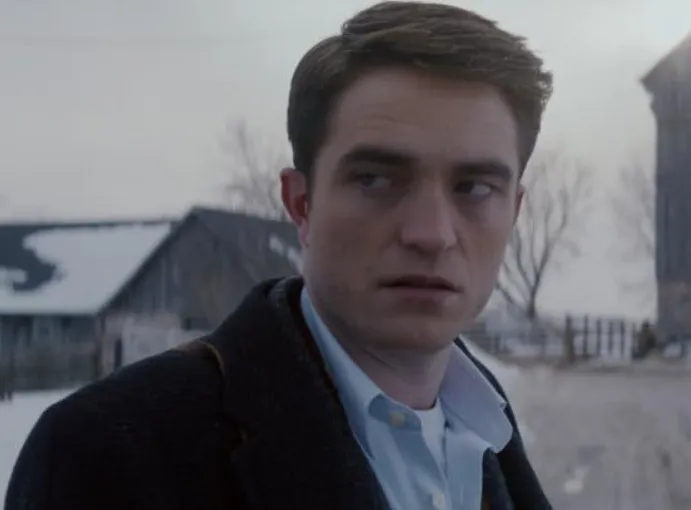 Robert Pattinson outdoors in a winter setting, wearing a coat and shirt, looking to the side with a serious expression.
