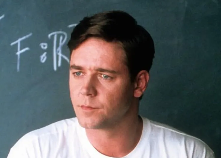 Russell Crowe looking thoughtful in a white shirt with a blackboard in the background, related to Freddie Mercury role discussion.