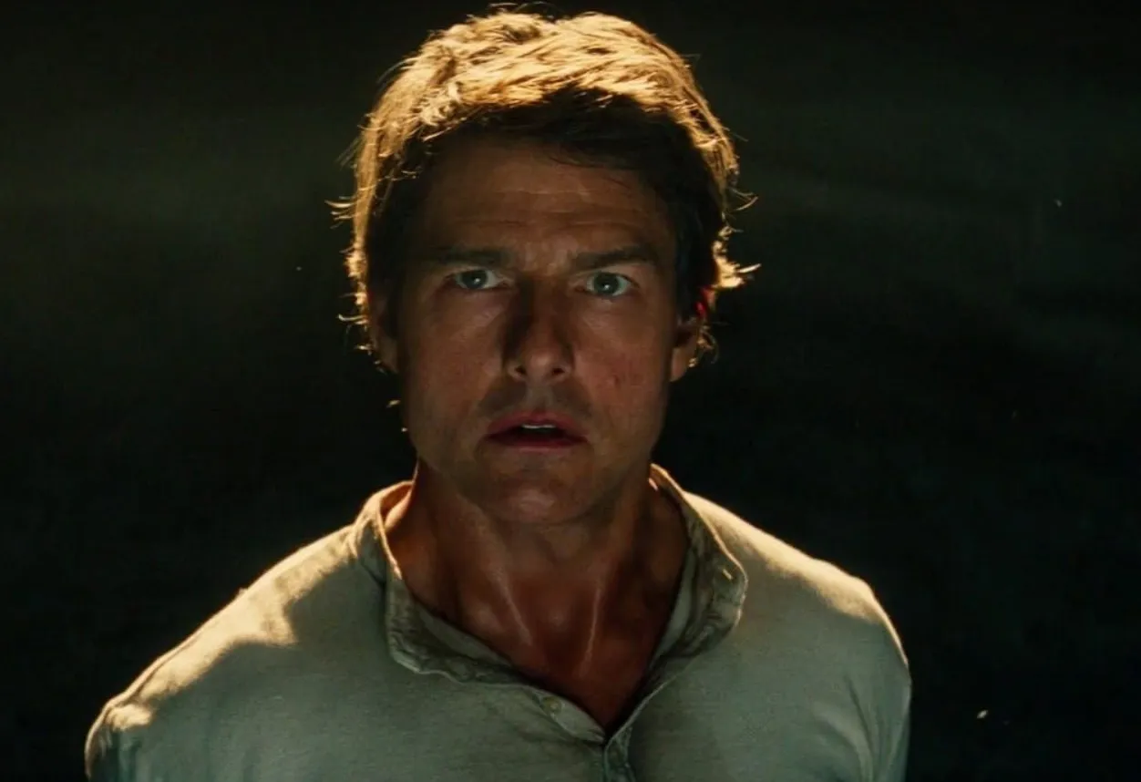 Tom Cruise in a Mission Impossible film scene, wearing a light shirt with intense expression in dim lighting.