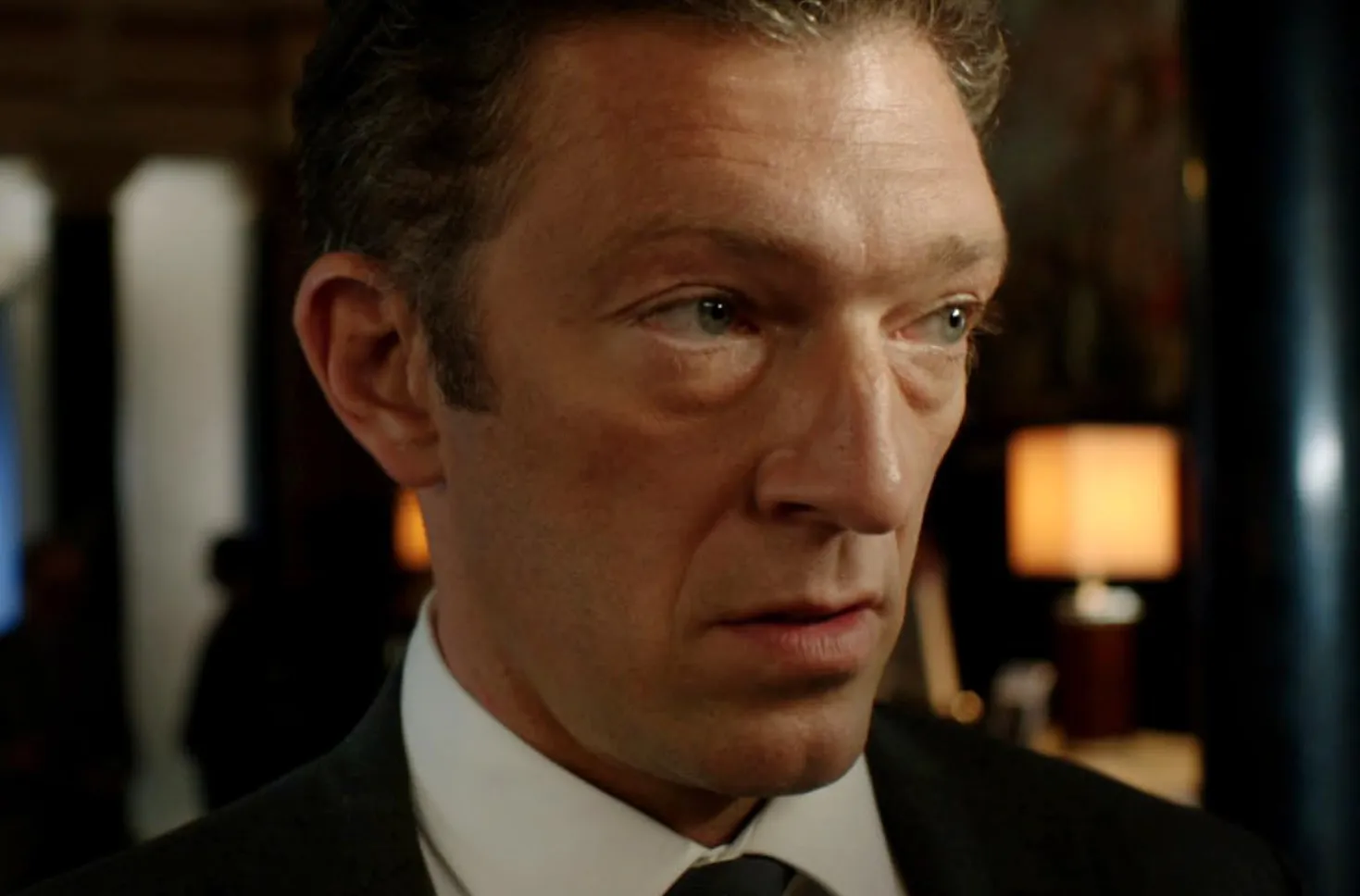 Vincent Cassel close-up in a suit, portraying a serious character in a scene from Fast & Furious films.