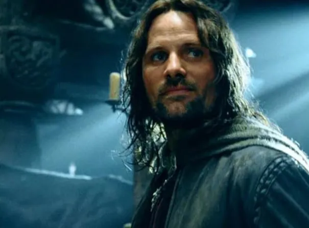 Actor Viggo Mortensen in a dark medieval setting, wearing a worn leather jacket and looking thoughtfully to the side.