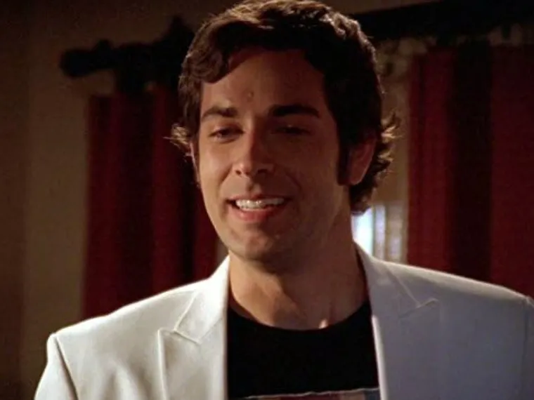 Zachary Levi smiling in a white jacket, featured as a main star in the High School Musical trilogy scene.