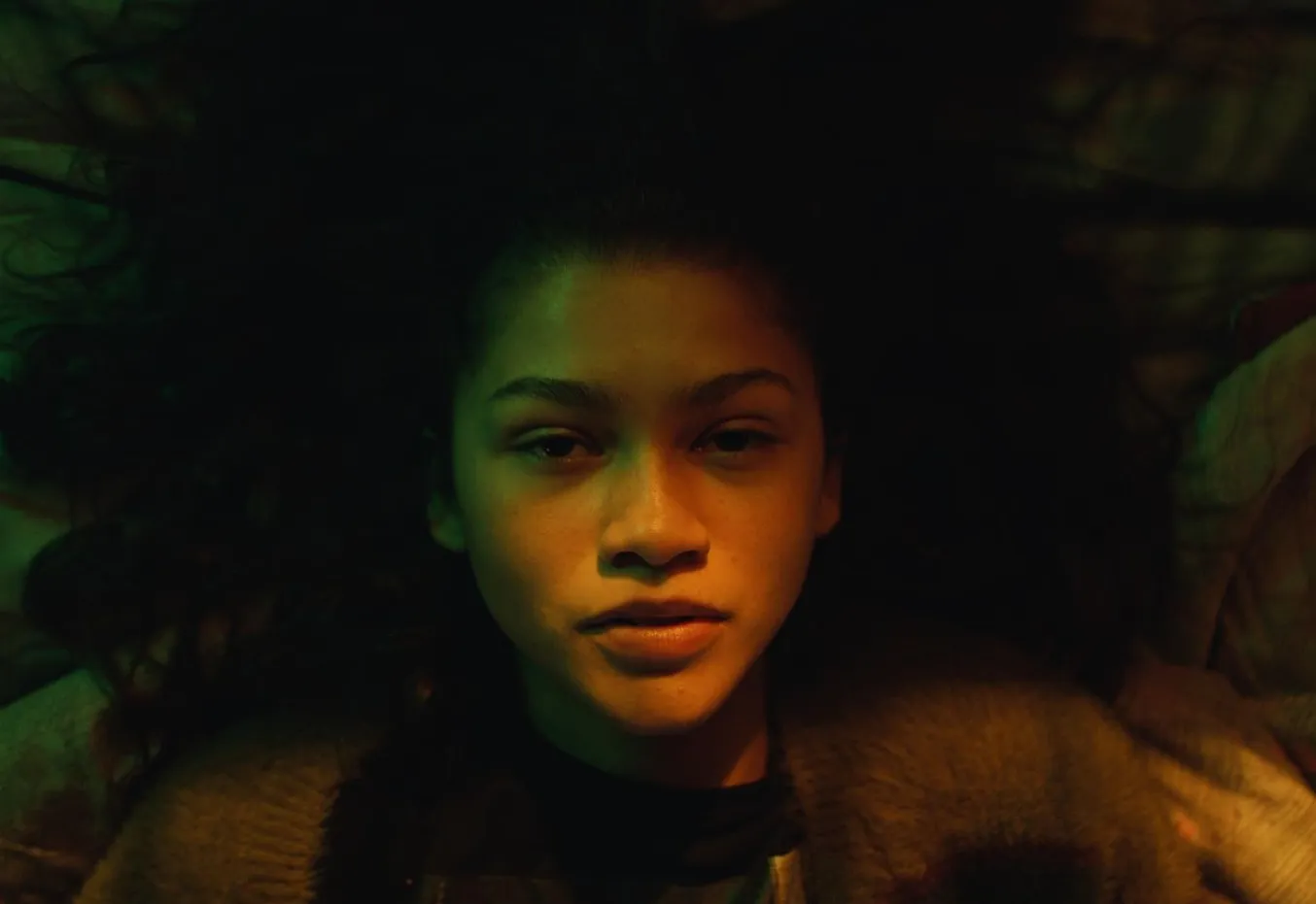 Zendaya lying down with hair spread out, dim lighting highlighting her face, portraying High School Musical star.