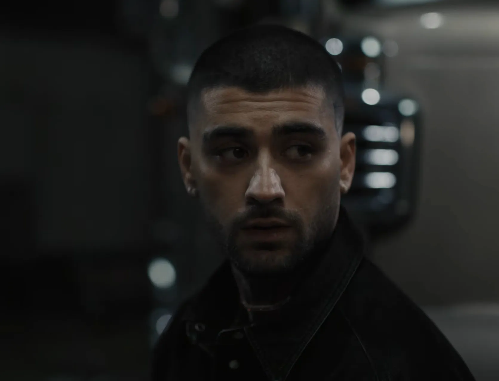 Zayn Malik looking away with intense expression in a dimly lit setting, creating strong eye contact effect.