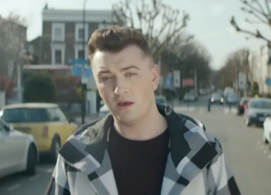 Sam Smith standing on a city street wearing a black and white checkered jacket, with focused eyes.