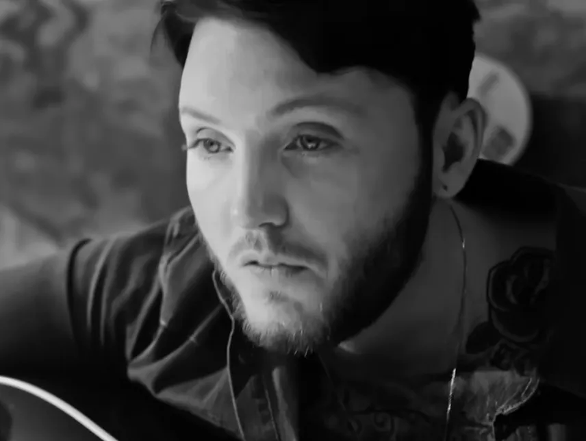 Close-up of James Arthur focused while playing guitar, highlighting his eyes and facial expression in black and white.