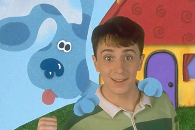 Steve and Blue from Blue’s Clues smiling in front of a colorful animated house on a nostalgic cartoon background.
