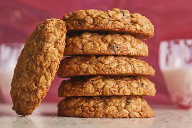 Stack of homemade oatmeal cookies on a marble surface with a blurred pink background, perfect for a potluck dessert.