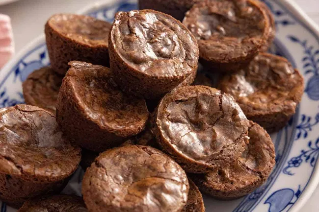 Brownie bites stacked on a blue and white patterned plate, showcasing their fudgy texture and chewy tops.